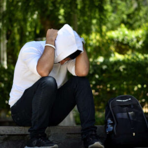 ಒತ್ತಡದಿಂದಾಗಿ ತಲೆಮೇಲೆ ಕೈ ಇಟ್ಟು ಕುಳಿತಿರುವ ಯುವಕ ಮತ್ತು ಒಂದು ಚೀಲವನ್ನು ಒಳಗೊಂಡ ಫೋಟೋ.  